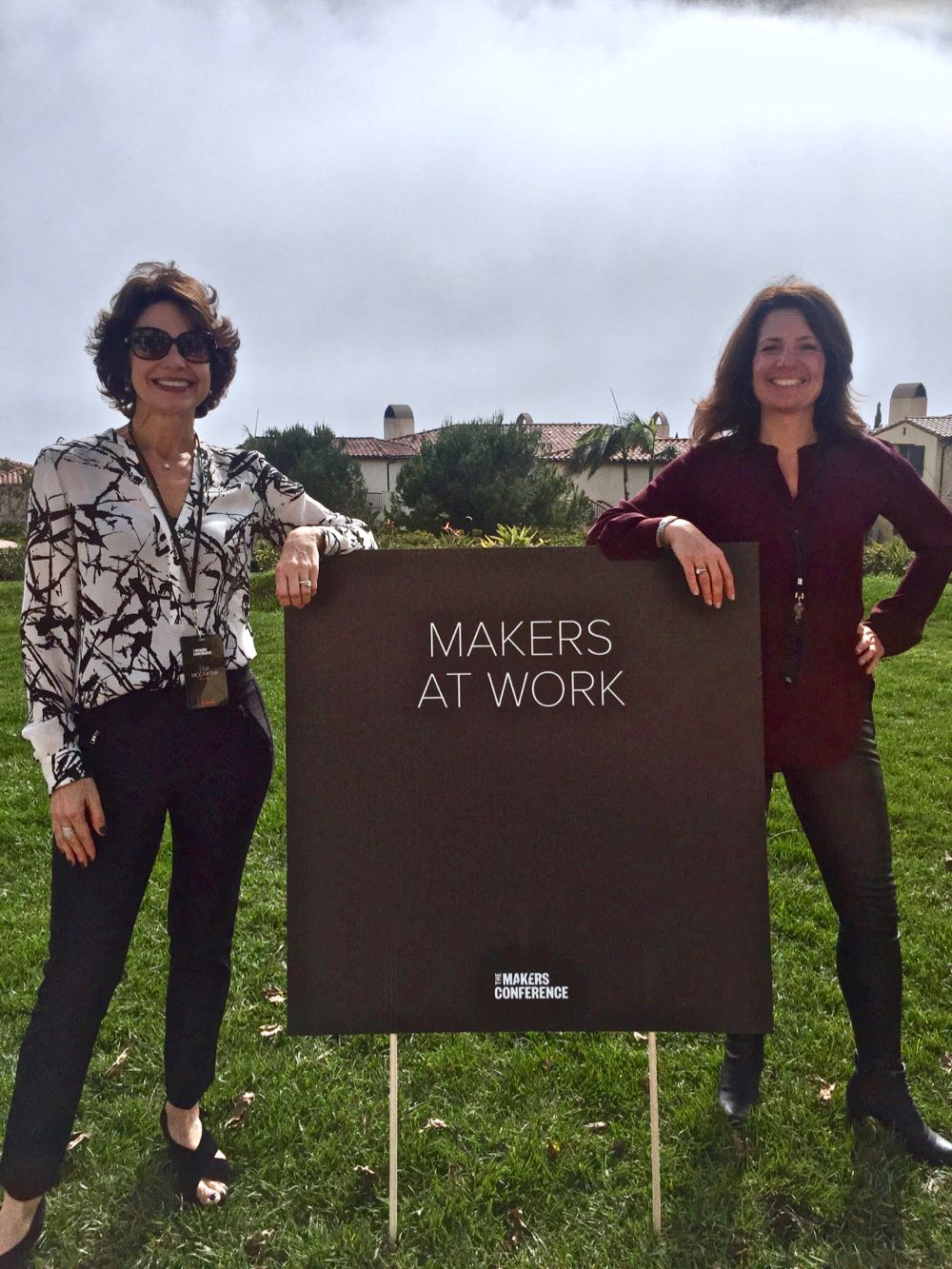Fast Forward Co-Founders Lisa McCarthy and Wendy Leshgold smile at the camera while standing by the Maker's Conference sign that says Makers at Work